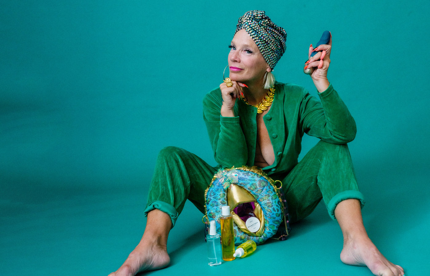 Lou on a green background in a green jumpsuit, with a vulva purse and holding the Deep Sea Blue STRONIC PETITE